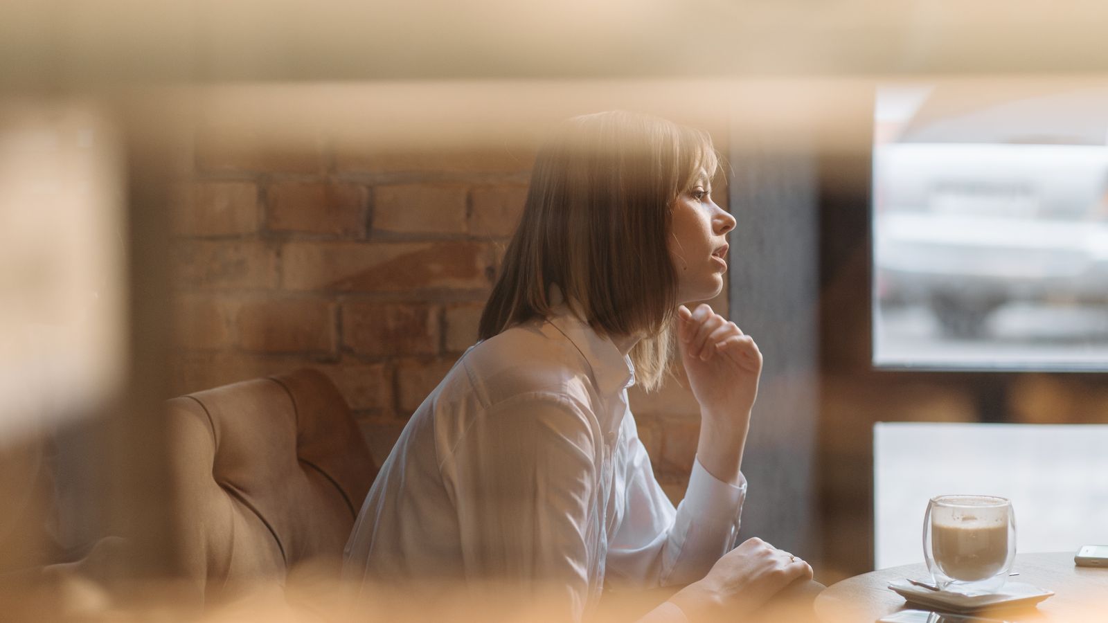 Woman seated beside a café window with a cup of coffee
