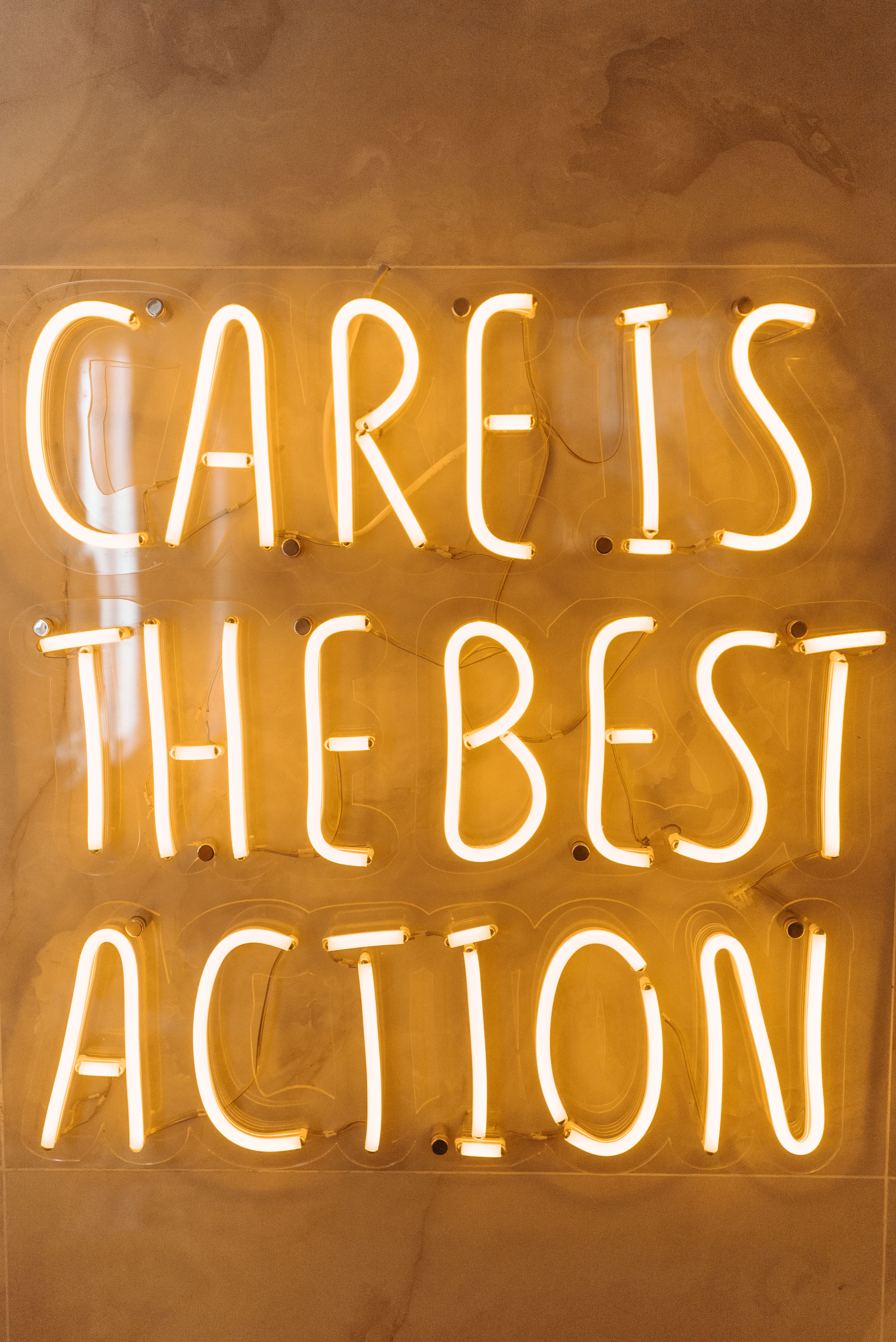 Bright neon sign declaring 'Care is the Best Action' in a stylish setup.