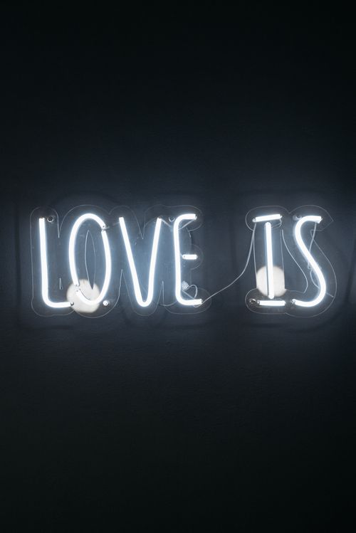 Free Glowing neon sign displaying 'Love Is' against a dark background, symbolizing affection. Stock Photo