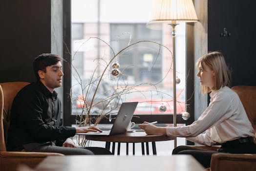 A young man and woman engaged in a business meeting with a laptop in a cozy cafe.