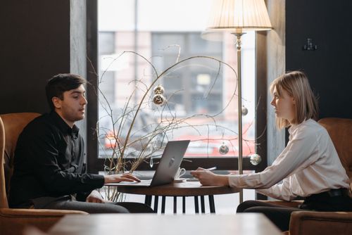 Free A young man and woman engaged in a business meeting with a laptop in a cozy cafe. Stock Photo