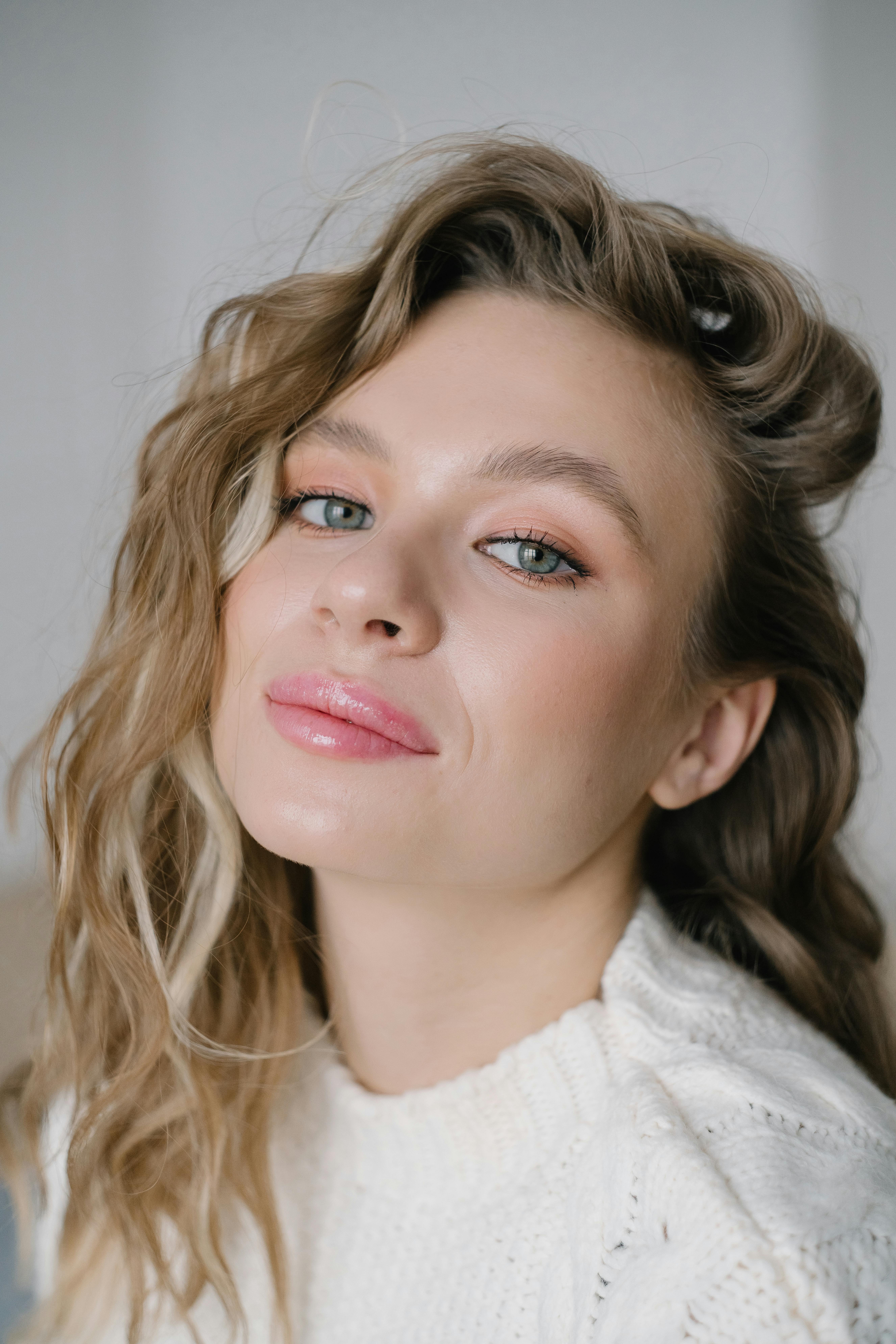 Elegant portrait shot of a woman with blonde wavy hair and subtle makeup, showcasing beauty and fashion.
