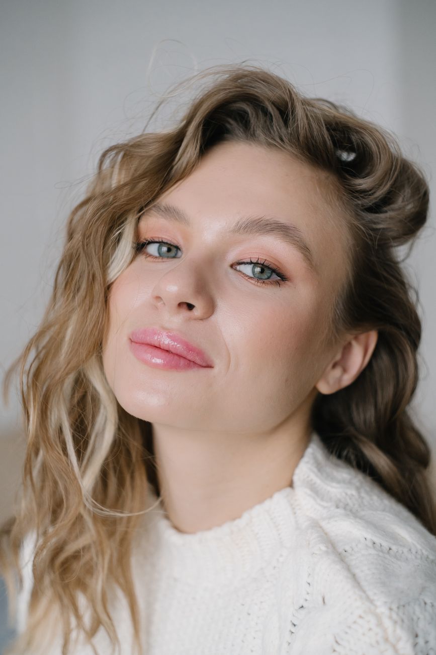 Elegant portrait shot of a woman with blonde wavy hair and subtle makeup, showcasing beauty and fashion.