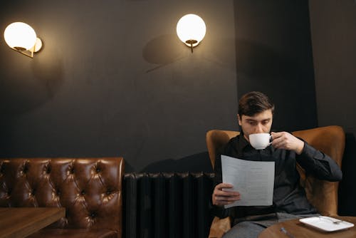 Man  in Black Long Sleeve Shirt Reading While Drinking Coffee