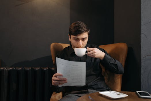 Man sipping coffee and reading a document in a cozy café setting.