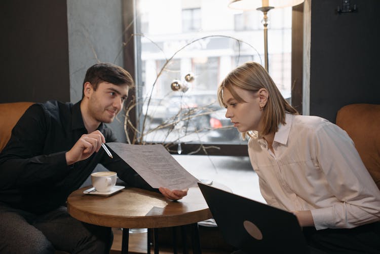 A Man Showing A Paper To A Woman Sitting Across