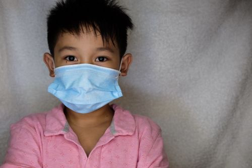 Free Young child wearing a blue face mask for protection during the pandemic, indoors. Stock Photo