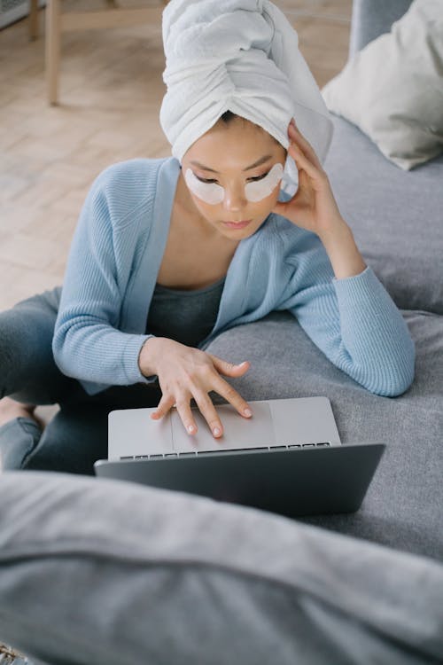 Free A Woman with Towel on Head and Under Eye Patch Using a Laptop Stock Photo