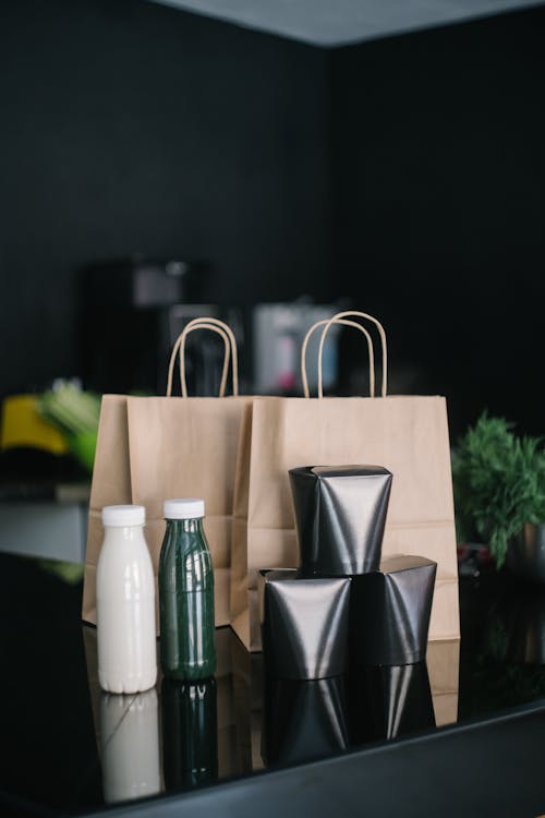 Paper Bags Beside Glass Bottles and Takeout Food on Black Table
