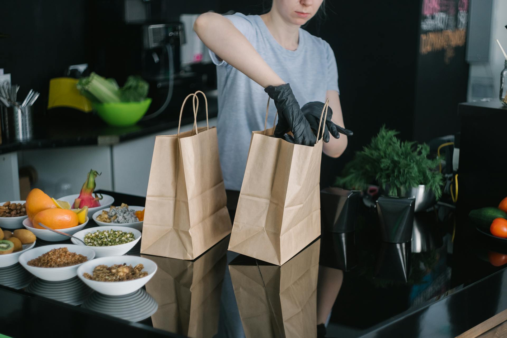 A person in a kitchen packing food ingredients into paper bags for takeout orders.
