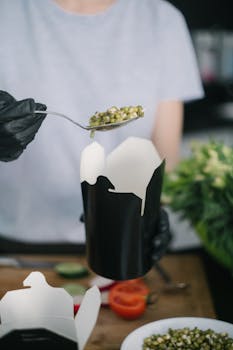 Close-up of a person scooping beans into a takeout box, showcasing fresh ingredients.