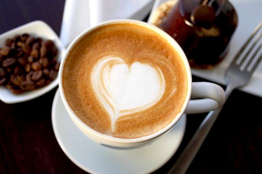 Creamy latte with heart art, surrounded by coffee beans and dessert. Perfect for cozy moments.