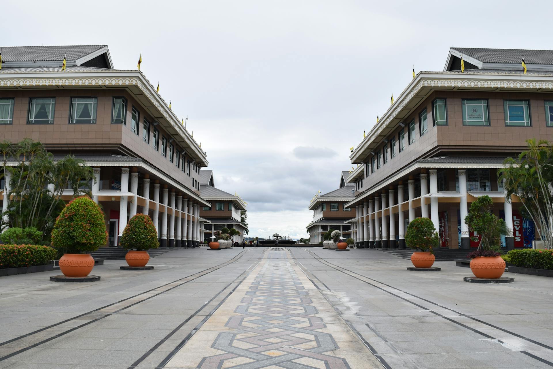 A view of symmetrical commercial buildings in a shopping area in Brunei with lush plants.