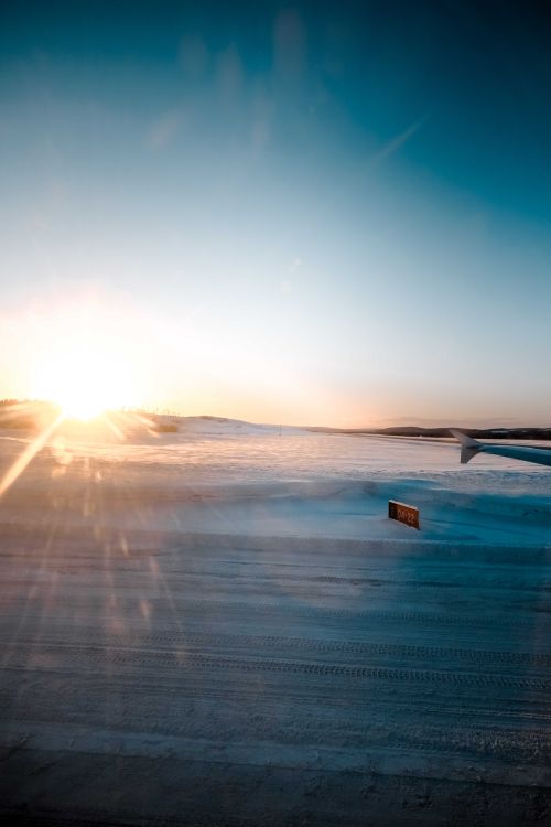 Free Through glass of wing of modern airplane driving on snowy airfield against cloudless sunset sky in winter Stock Photo