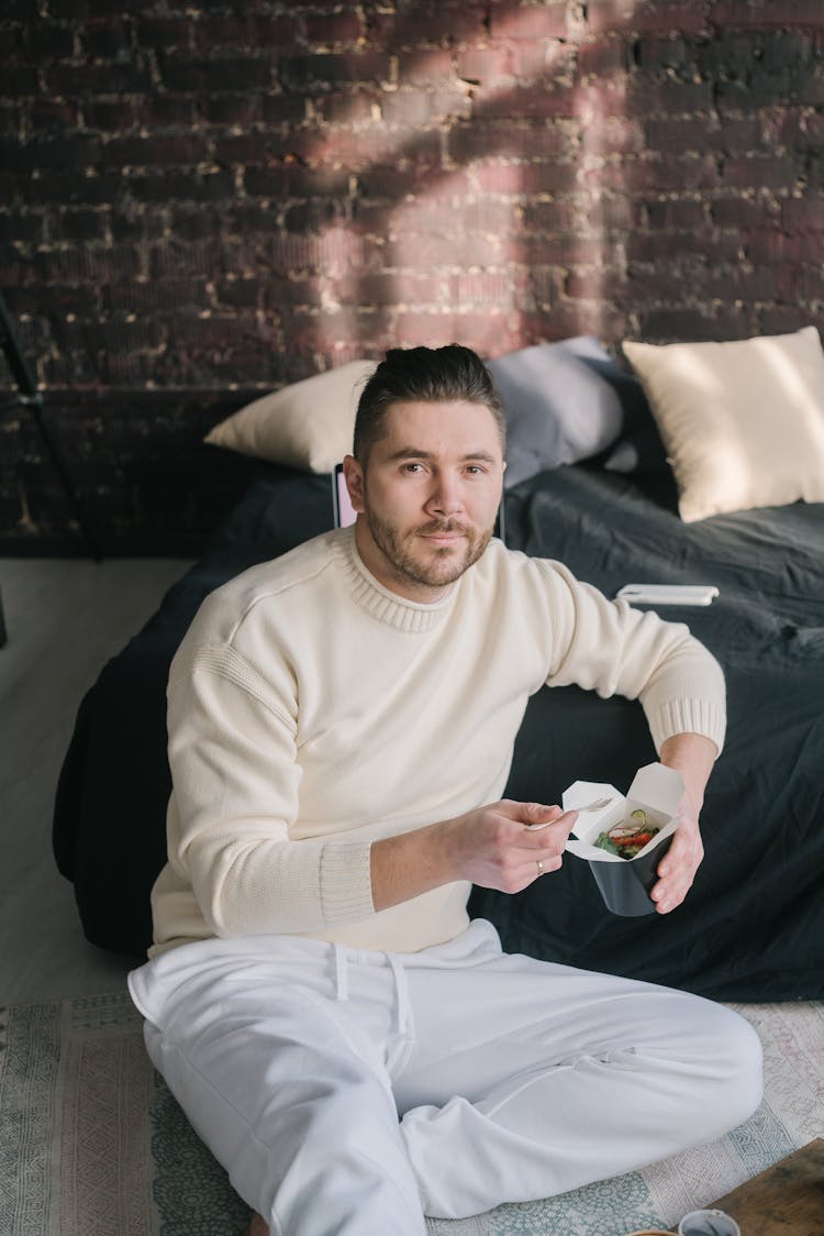 A Man Sitting Beside Bed Holding A Take Out Box