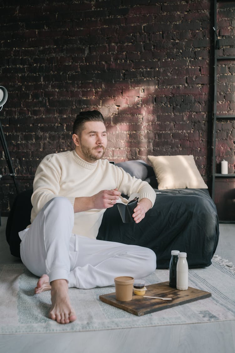 Bearded Man In White Sweater Sitting On Floor Eating Take Out Food