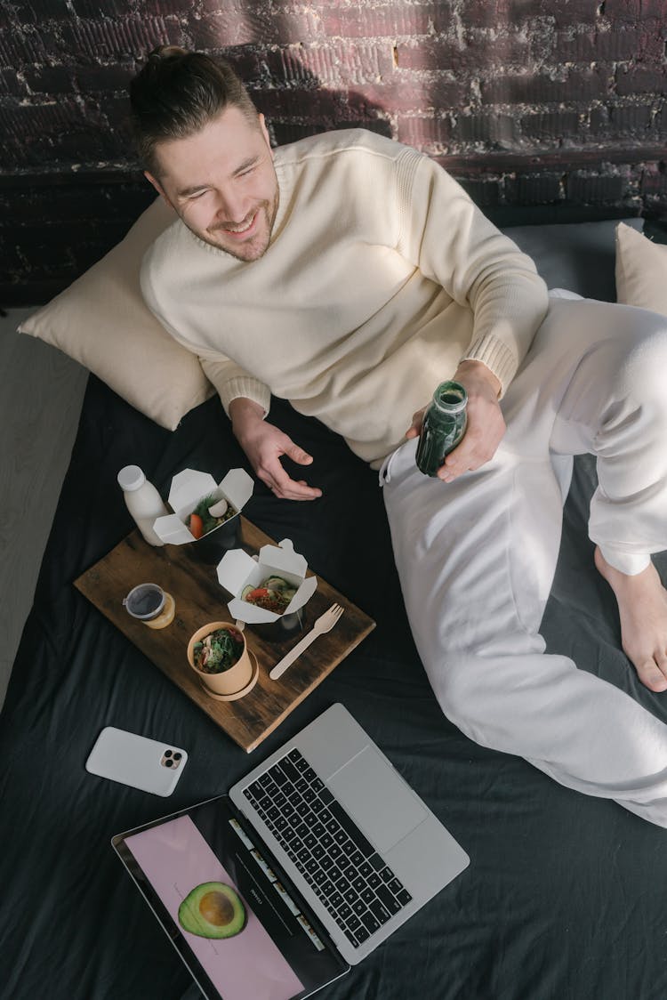 A Man Lying On Bed Holding A Bottle Of Drink