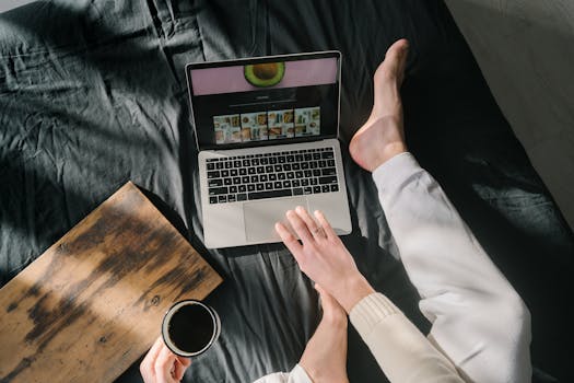 A relaxing scene showing a person using a laptop while holding coffee on a bed.