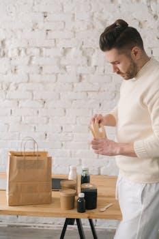 Man packing eco-friendly containers on a wooden table with a white brick background indoors.