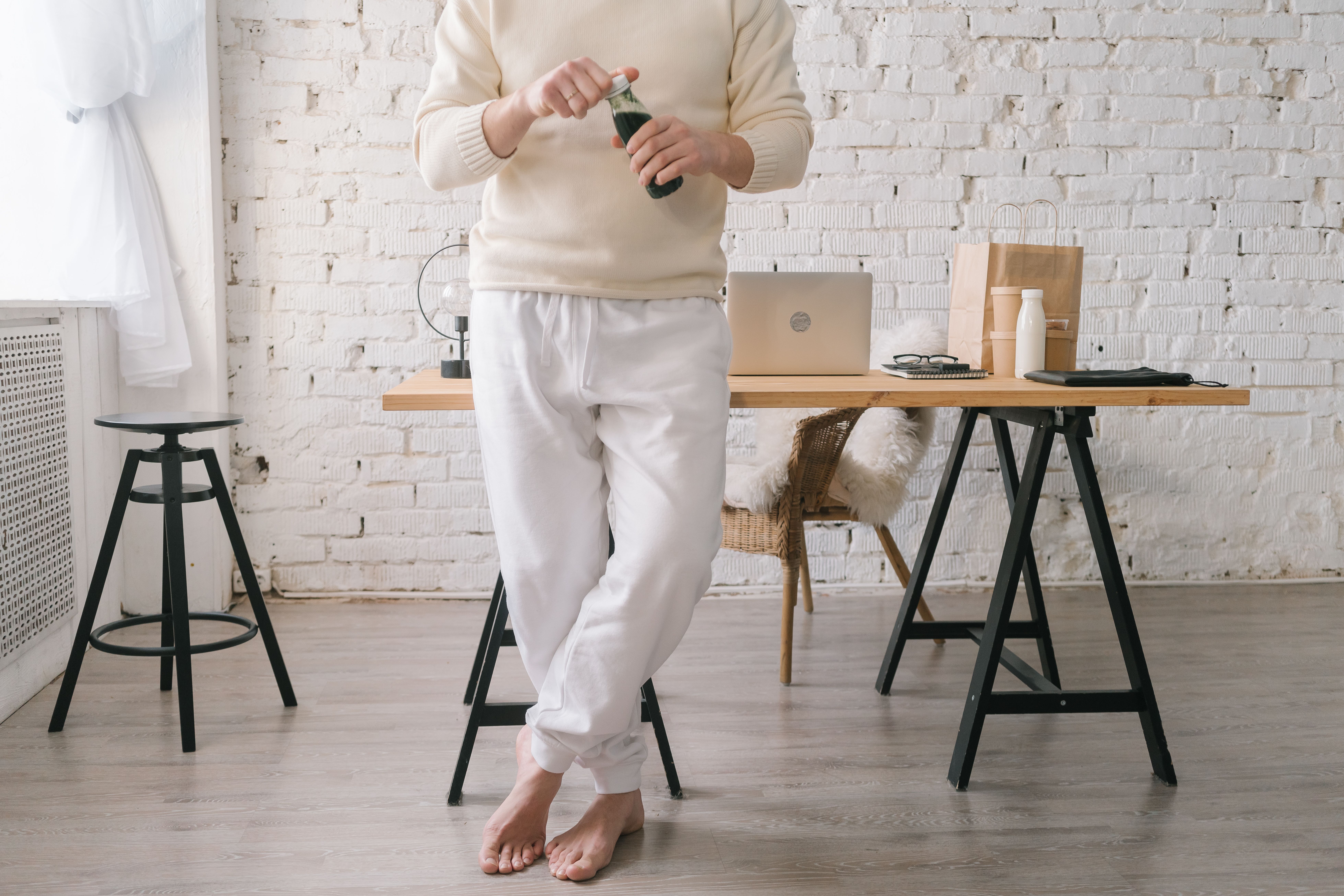 Barefoot man enjoying a drink in a cozy home office setting, showcasing a relaxed lifestyle.