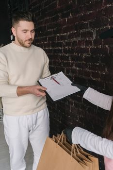 A man accepts a delivery package and signs a clipboard indoors.