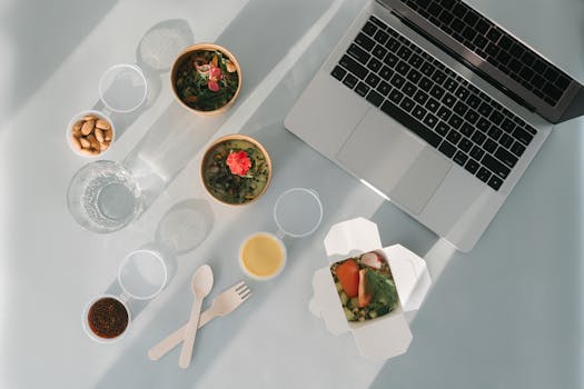Flat lay of a healthy lunch set with laptop, almonds, and soup bowls, ideal for work-from-home lifestyle.