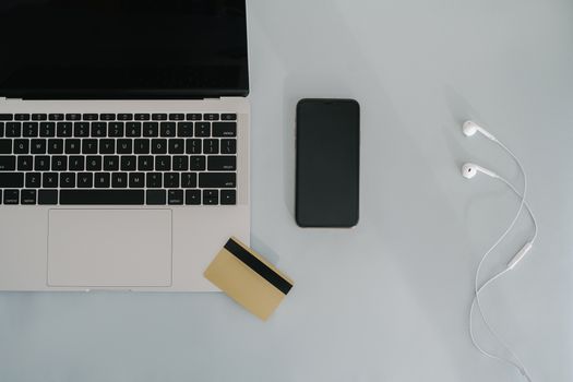 Flat lay of laptop, smartphone, and earphones with credit card on a desk.