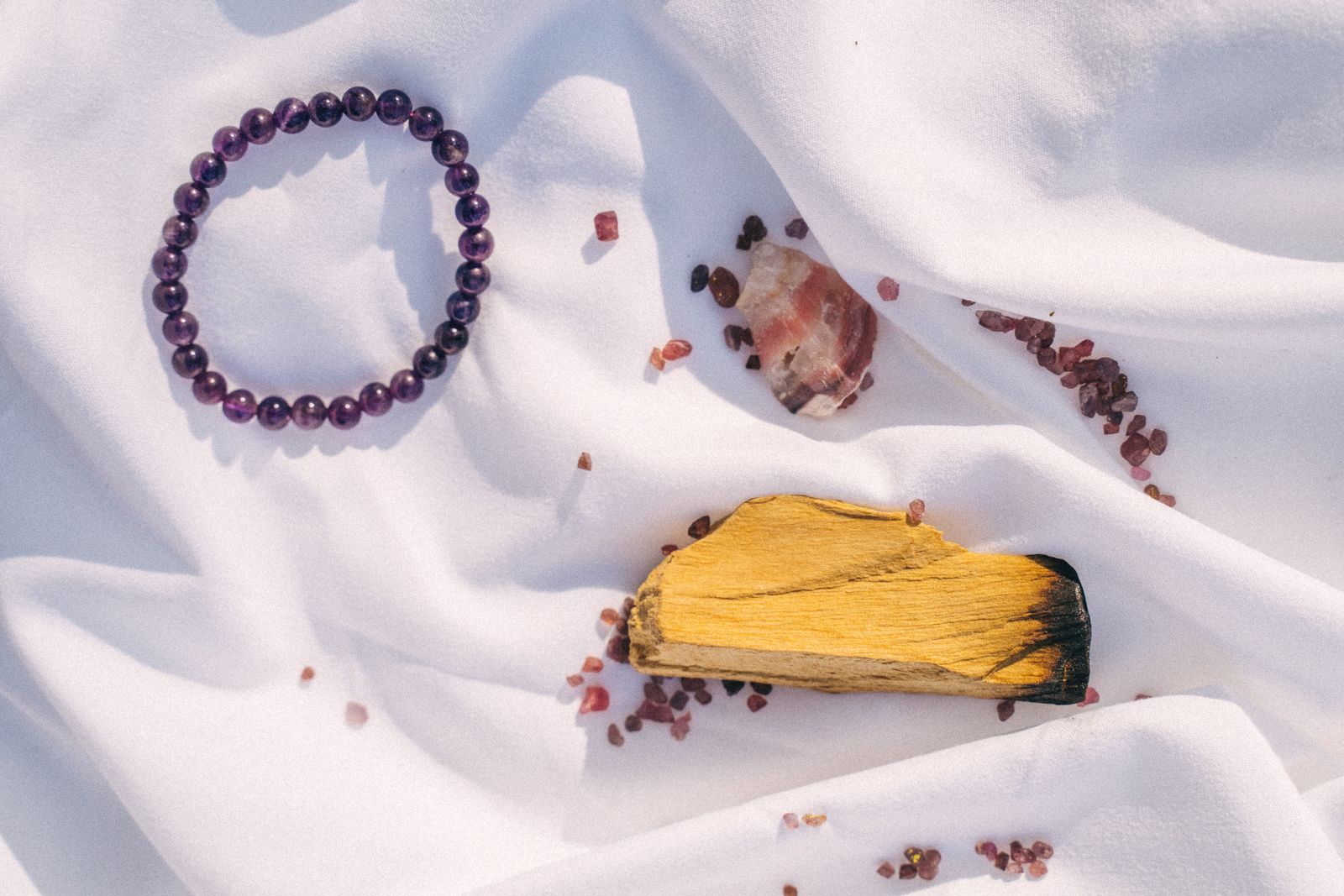 Amethyst crystal bracelet arranged with palo santo sticks and crystals on white fabric