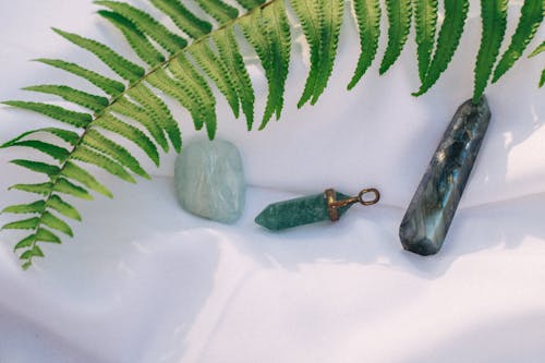 Healing Crystals Beside Green Fern Leaf on a White Fabric