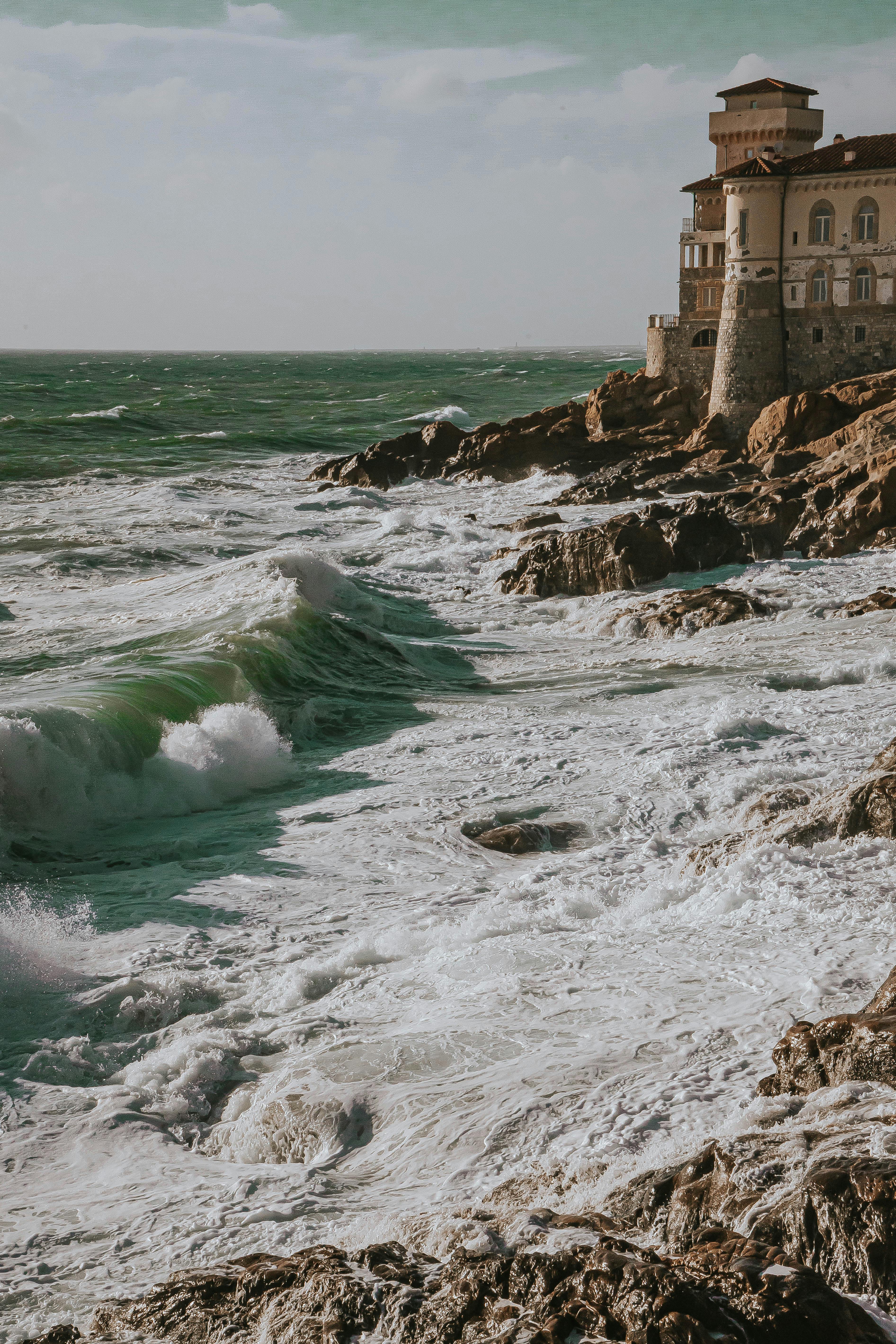 Powerful waves crash against the rocky seashore by a castle in Livorno, Tuscany.