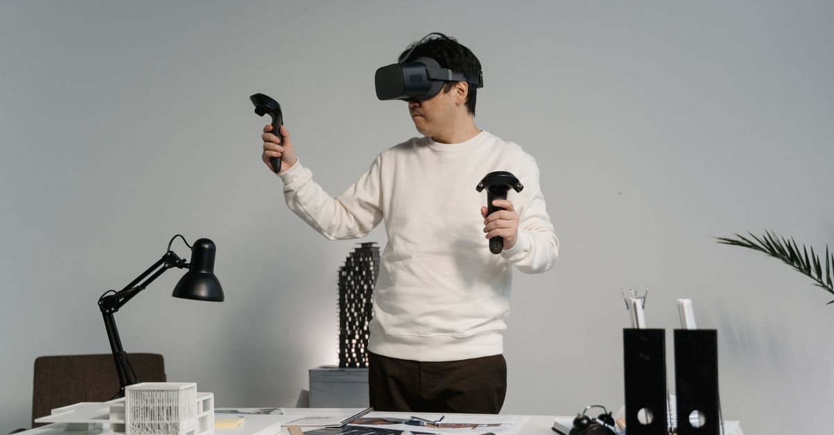 Adult man in workspace using VR headset and controllers, engaging with virtual reality experience.