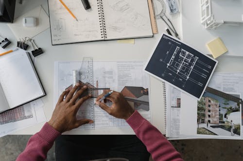 Free Architect designing plans at a desk surrounded by tools, drafts, and blueprints. Stock Photo