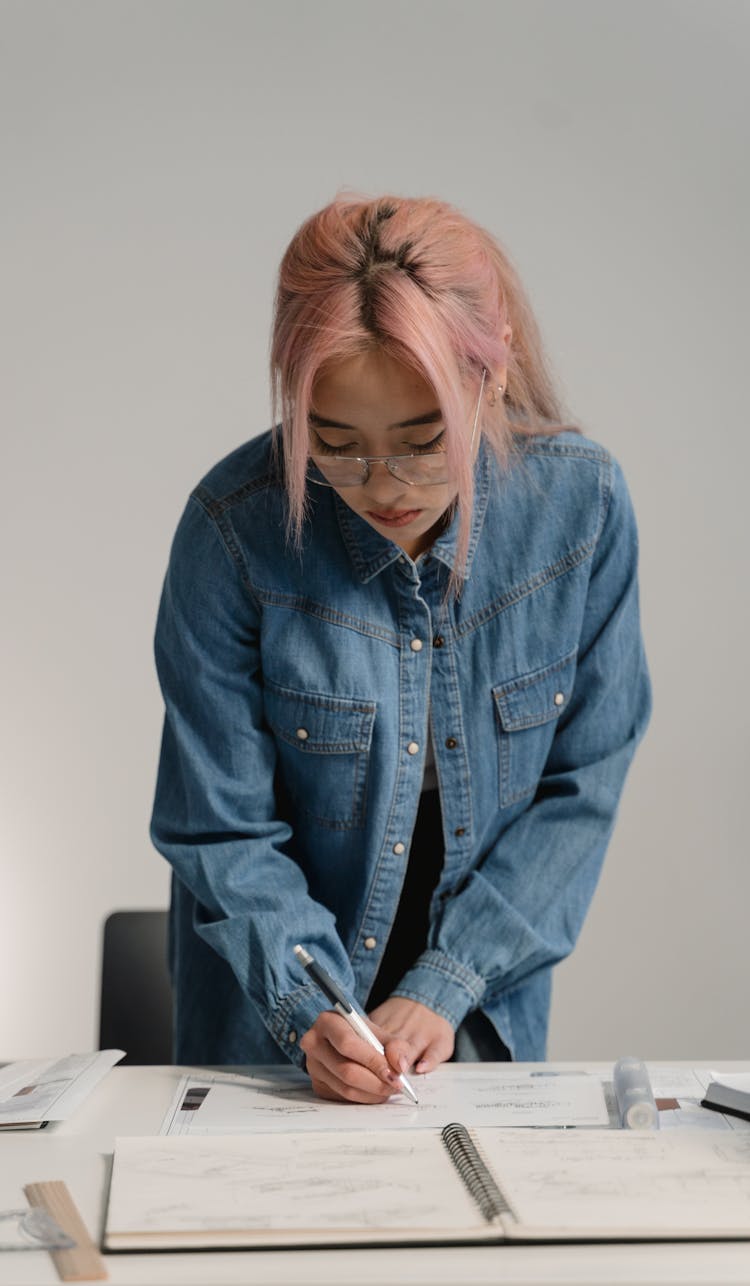 A Woman With Pink Hair Wearing Denim Jacket Writing On Bond Paper