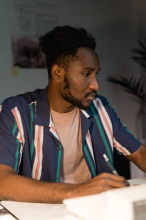 Free A young adult with facial hair working attentively at a desk inside a dimly lit room. Stock Photo