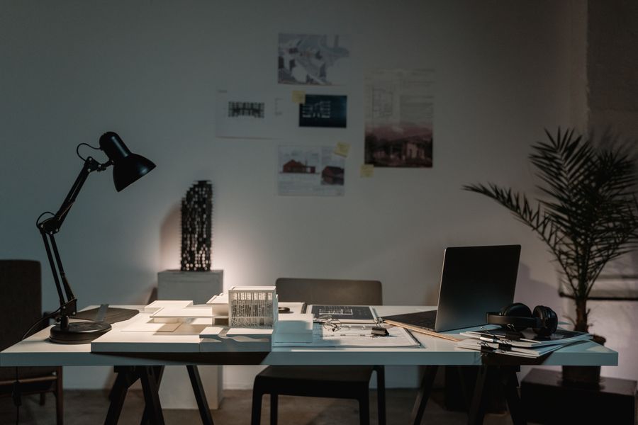 A contemporary architect's desk with design plans, laptop, and lamp in a spacious office.