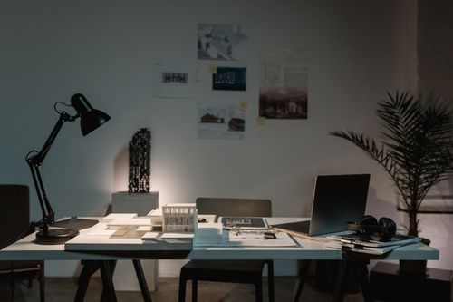 Free A contemporary architect's desk with design plans, laptop, and lamp in a spacious office. Stock Photo