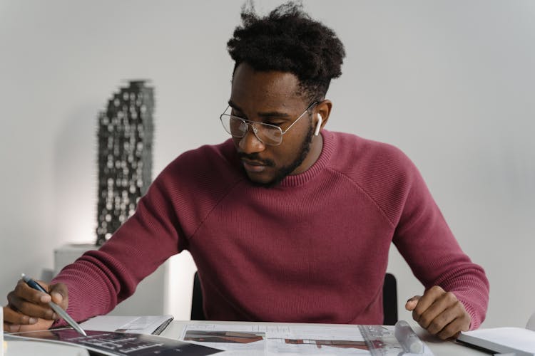 A Man In Sweater Wearing Bluetooth Headset While Working On His Table