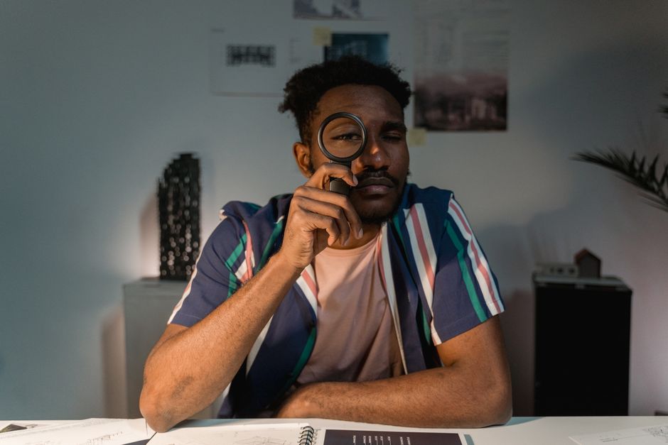 A contemplative man holding a magnifying glass at a table indoors. A contemplative man holding a magnifying glass at a table indoors.