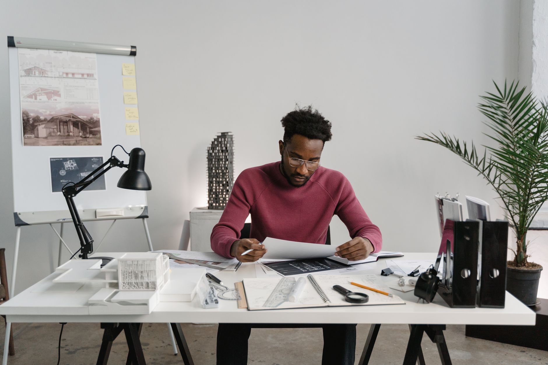 Architect working on designs at a desk cluttered with planning materials and tools. (Photo by Tima Miroshnichenko on Pexels)