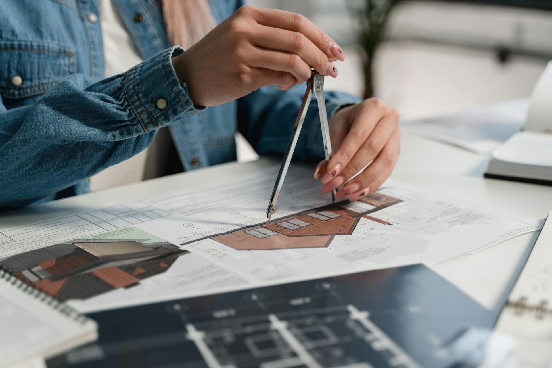 A creative professional using a compass on blueprints at an office desk.