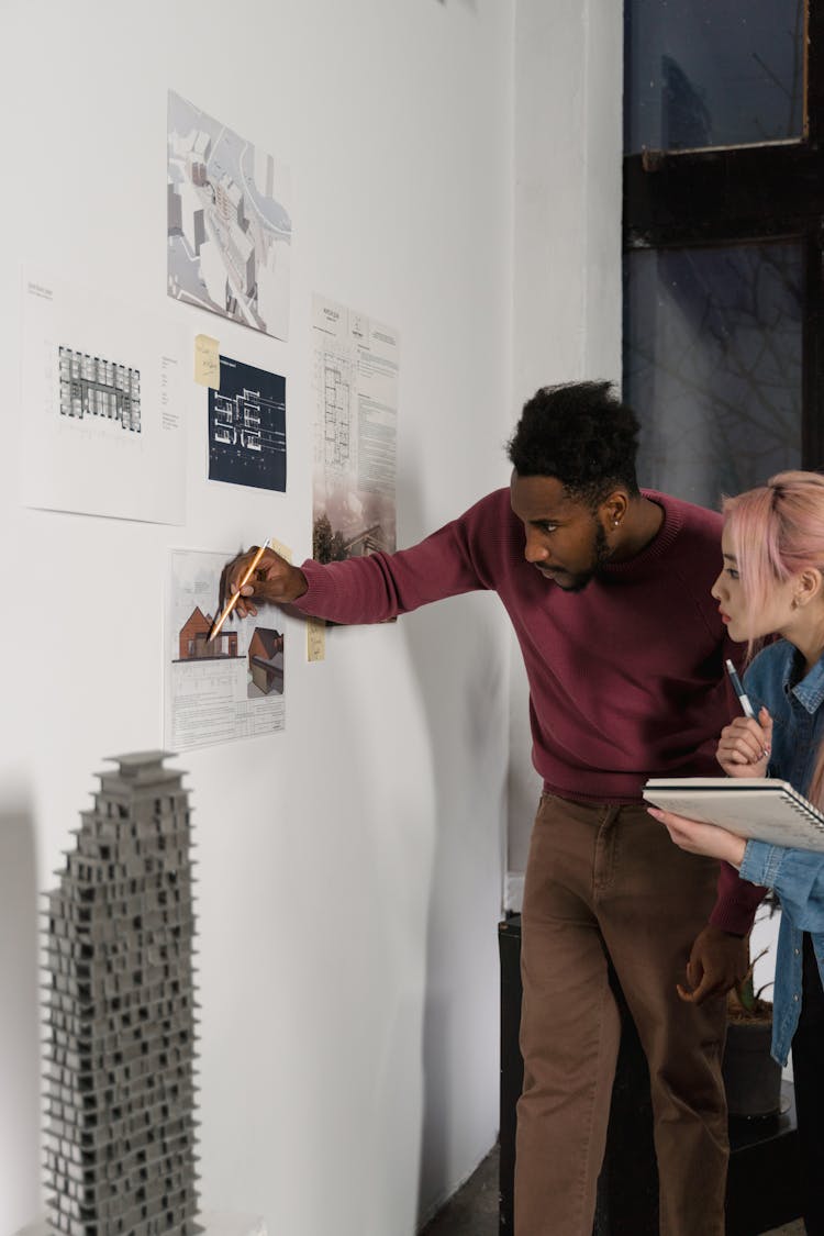 A Man And A Woman Checking The Printed Paper Posted On The Wall