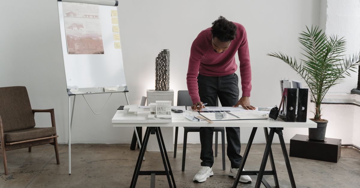 An architect stands at a desk in a modern office, examining blueprints for a project.