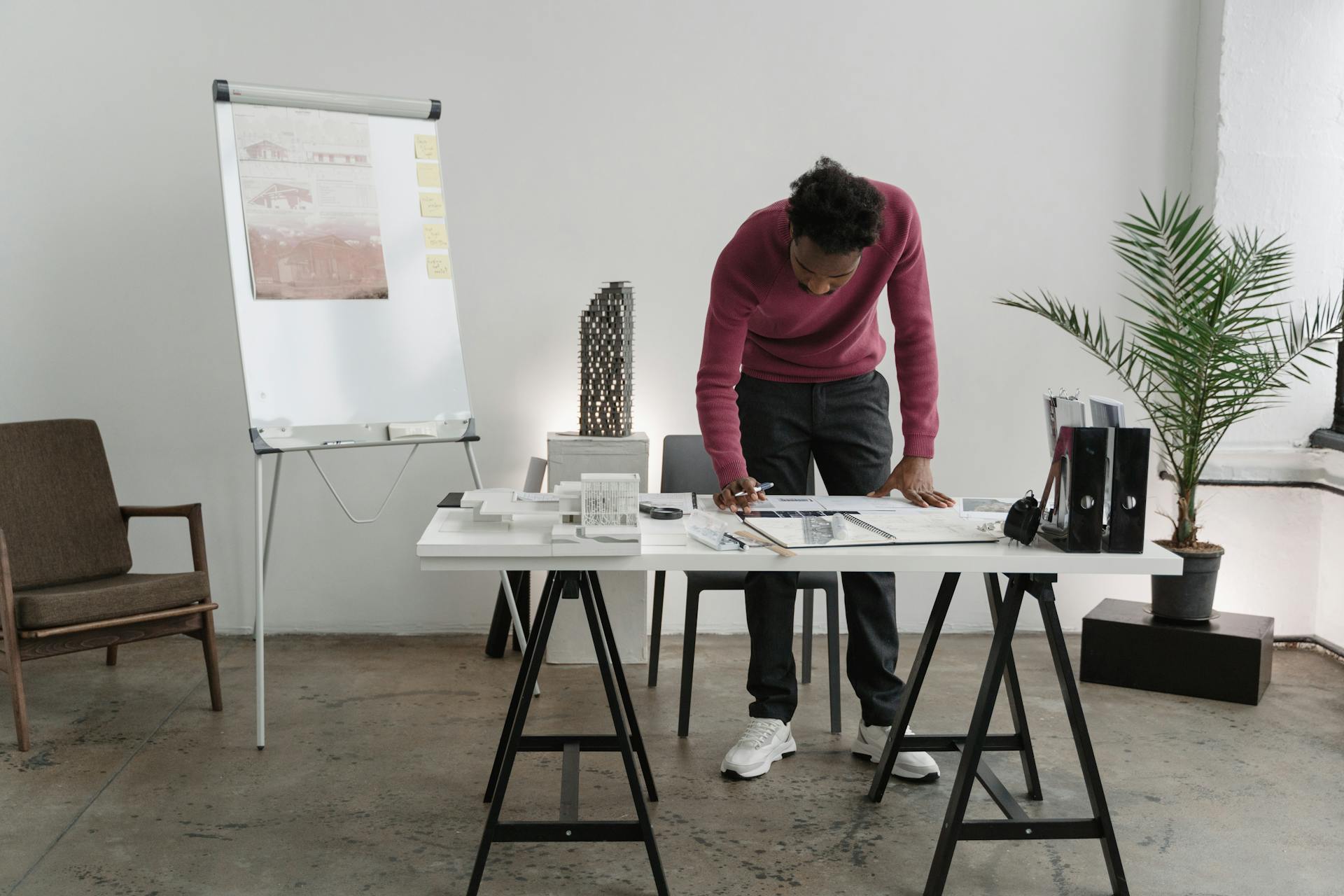 An architect stands at a desk in a modern office, examining blueprints for a project.