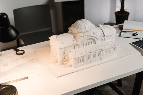 Free A detailed architectural model displayed on a designer's desk with drawing tools and documents. Stock Photo