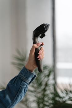A close-up of a hand holding a handheld device indoors, against a blurred background.
