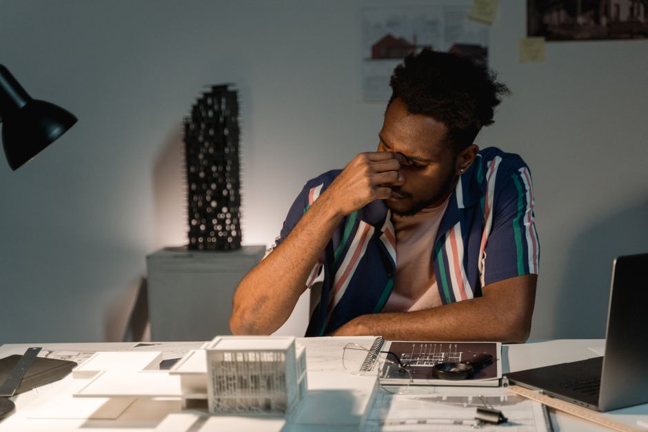 Tired architect working at night on architectural models and design plans.