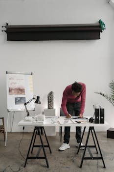 Architect in a pink sweater working on blueprints at a desk in a contemporary office.
