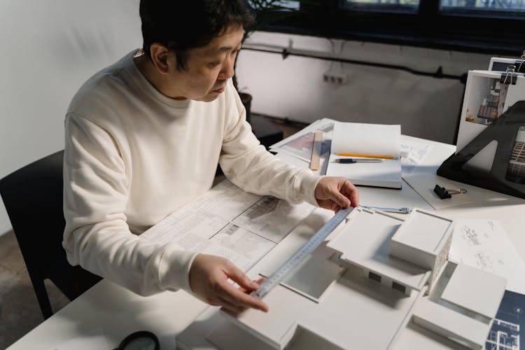 Man In White Long Sleeve Shirt Getting Measurement Of A Scale Model With Ruler