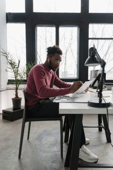 A professional architect concentrates on sketching designs at a modern desk in an office.