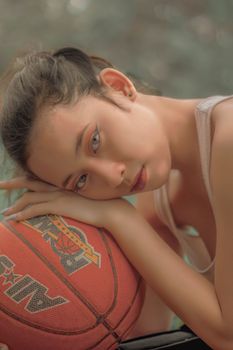 A young woman rests thoughtfully on a basketball, showcasing serene beauty and sports theme.